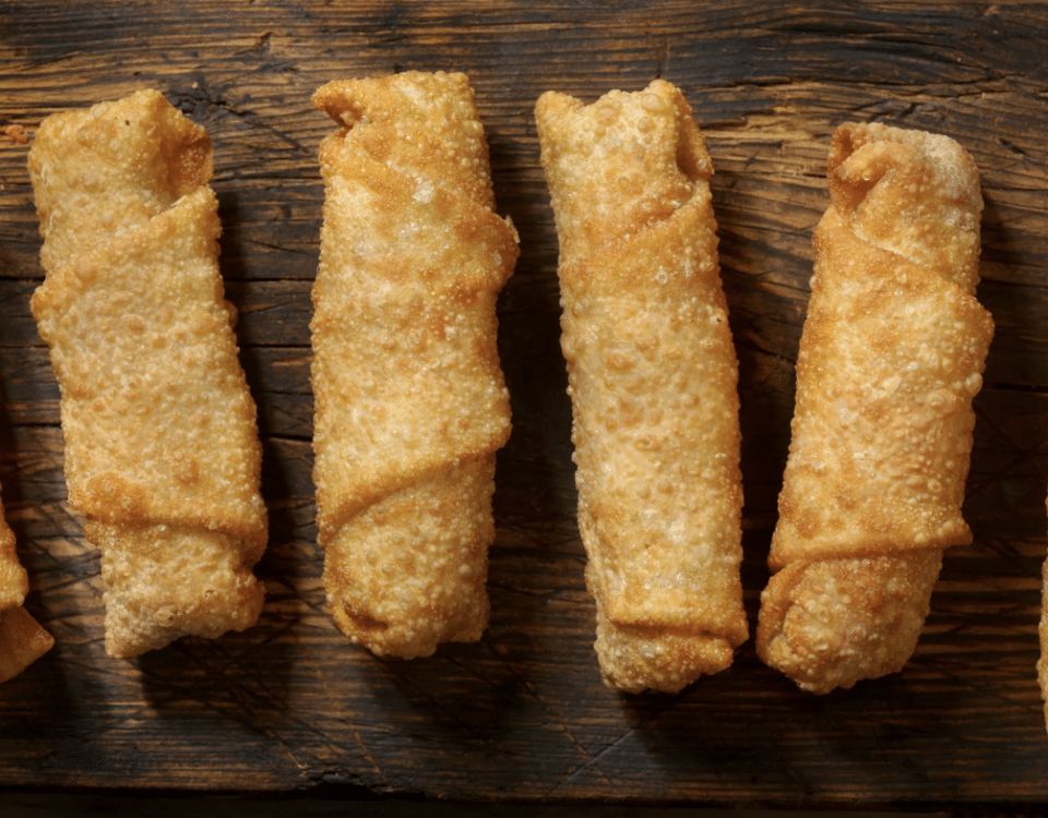 close up of several egg rolls lined up on a wood table